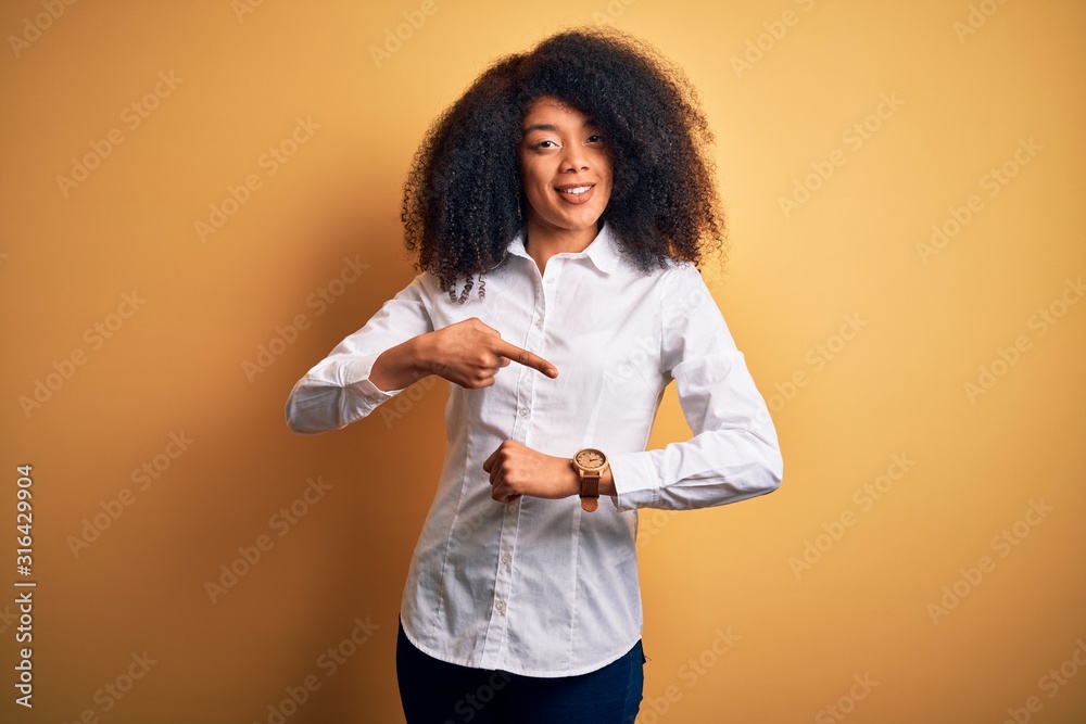 Young beautiful african american elegant woman with afro hair standing over yellow background In hurry pointing to watch time, impatience, upset and angry for deadline delay Young beautiful african american elegant woman with afro hair standing over yellow background In hurry pointing to watch time, impatience, upset and angry for deadline delay