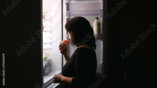 A woman opens the fridge door to take the cake.On a black background.