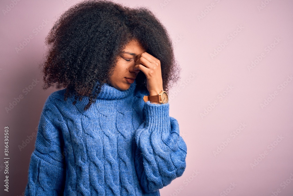 Young beautiful african american woman with afro hair wearing winter sweater over pink background tired rubbing nose and eyes feeling fatigue and headache. Stress and frustration concept. Young beautiful african american woman with afro hair wearing winter sweater over pink background tired rubbing nose and eyes feeling fatigue and headache. Stress and frustration concept.