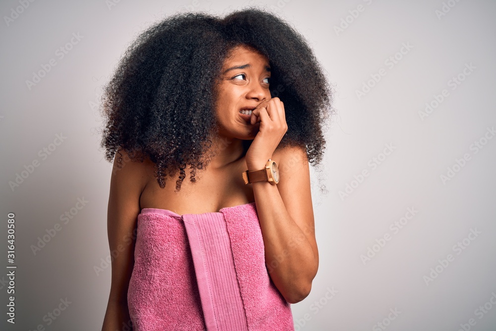 Young african american woman with afro hair wearing a body towel after beauty care shower looking stressed and nervous with hands on mouth biting nails. Anxiety problem. Young african american woman with afro hair wearing a body towel after beauty care shower looking stressed and nervous with hands on mouth biting nails. Anxiety problem.