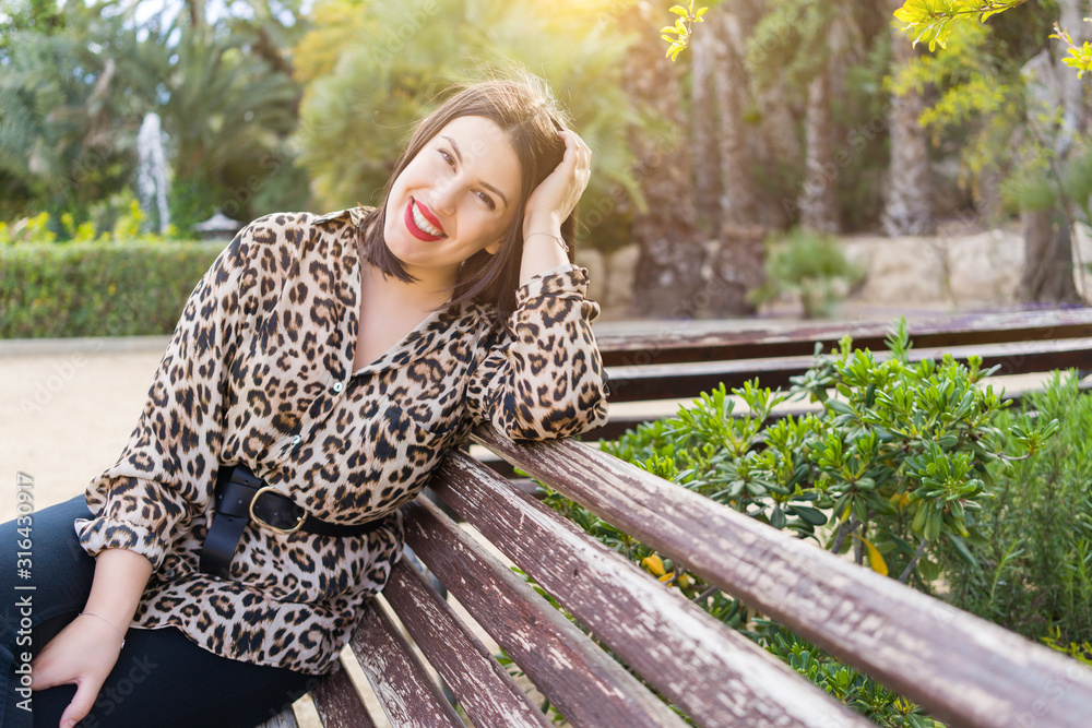 Young beautiful woman with red lips smiling happy sitting on a bench at garden Young beautiful woman with red lips smiling happy sitting on a bench at garden