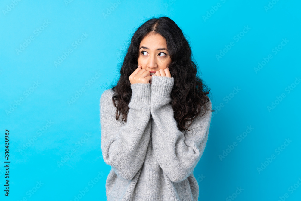 Spanish Chinese woman over isolated blue background nervous and scared putting hands to mouth Spanish Chinese woman over isolated blue background nervous and scared putting hands to mouth