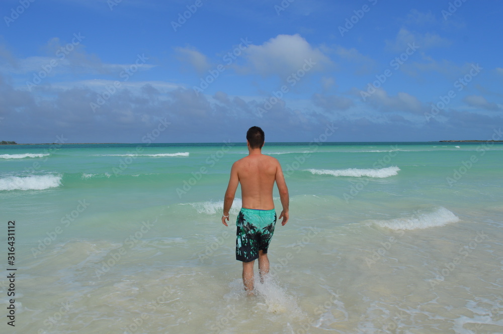 Young handsome guy is walking on a tropical white sand beach and watching waves in Cayo Coco, Cuba 