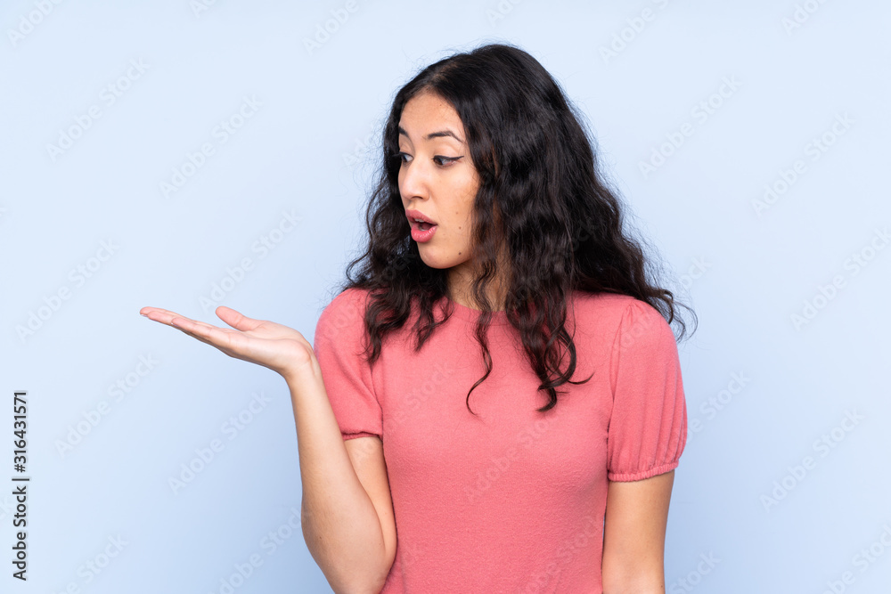 Mixed race woman wearing a sweater over isolated blue background holding copyspace imaginary on the palm Mixed race woman wearing a sweater over isolated blue background holding copyspace imaginary on the palm