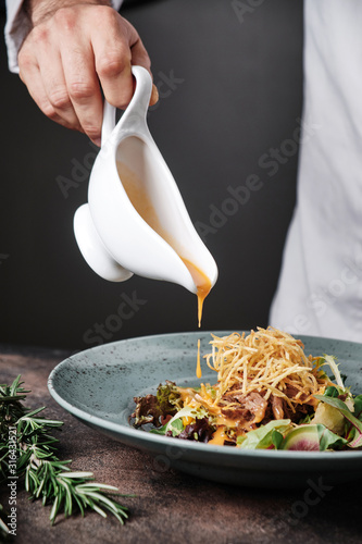 Chef plating up food in a restaurant pouring a gravy or sauce over the meat salad with potato