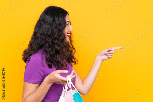 Spanish Chinese woman with shopping bag over isolated background pointing to the side to present a product