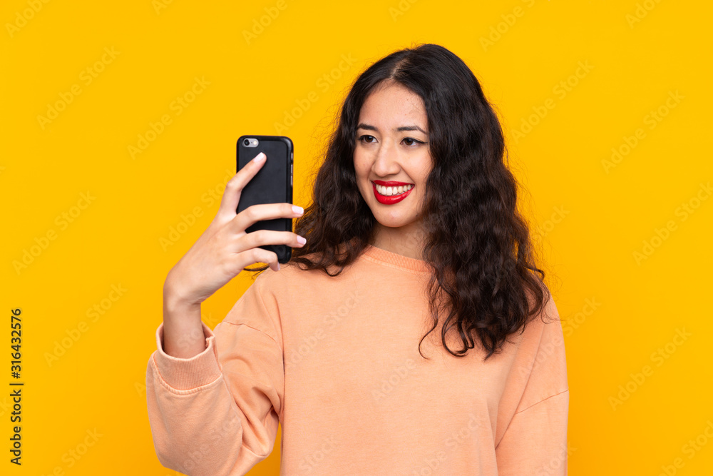 Spanish Chinese woman over isolated yellow background making a selfie Spanish Chinese woman over isolated yellow background making a selfie