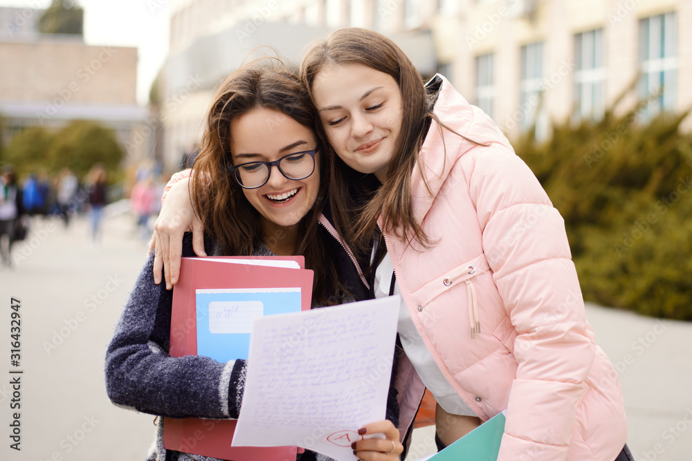 Happy female students with excellent test result. Two best friends passed examination and received A grade for their work Happy female students with excellent test result. Two best friends passed examination and received A grade for their work