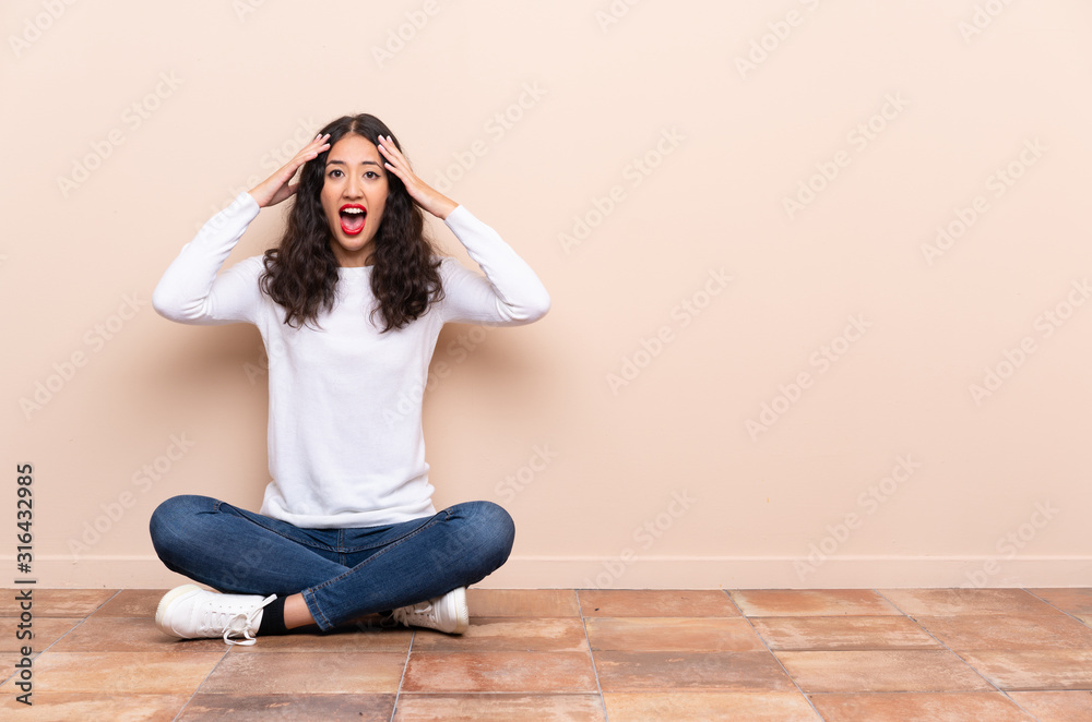 Young woman sitting on the floor with surprise expression Young woman sitting on the floor with surprise expression