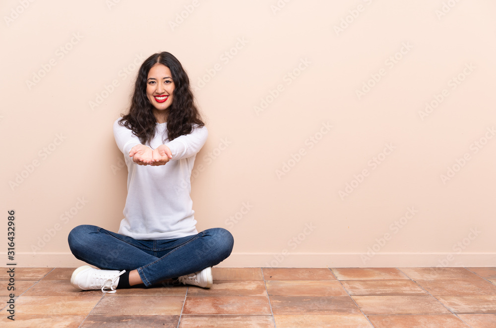 Young woman sitting on the floor holding copyspace imaginary on the palm to insert an ad Young woman sitting on the floor holding copyspace imaginary on the palm to insert an ad