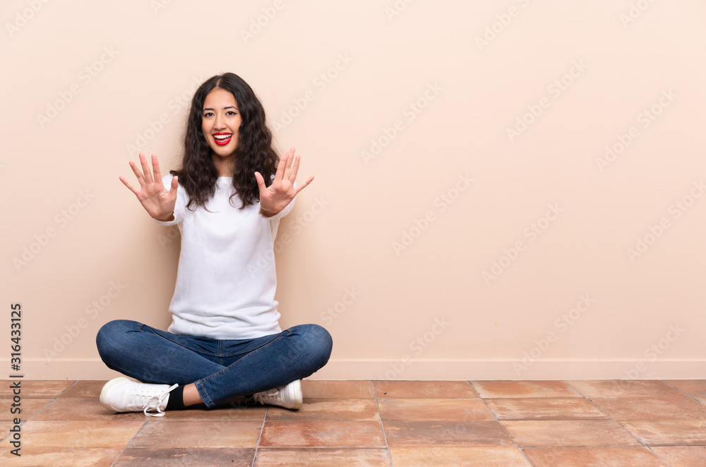 Young woman sitting on the floor counting ten with fingers Young woman sitting on the floor counting ten with fingers