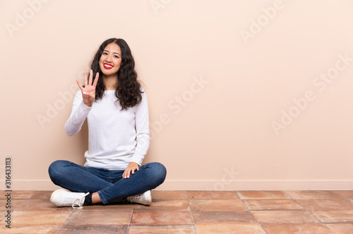 Young woman sitting on the floor happy and counting four with fingers