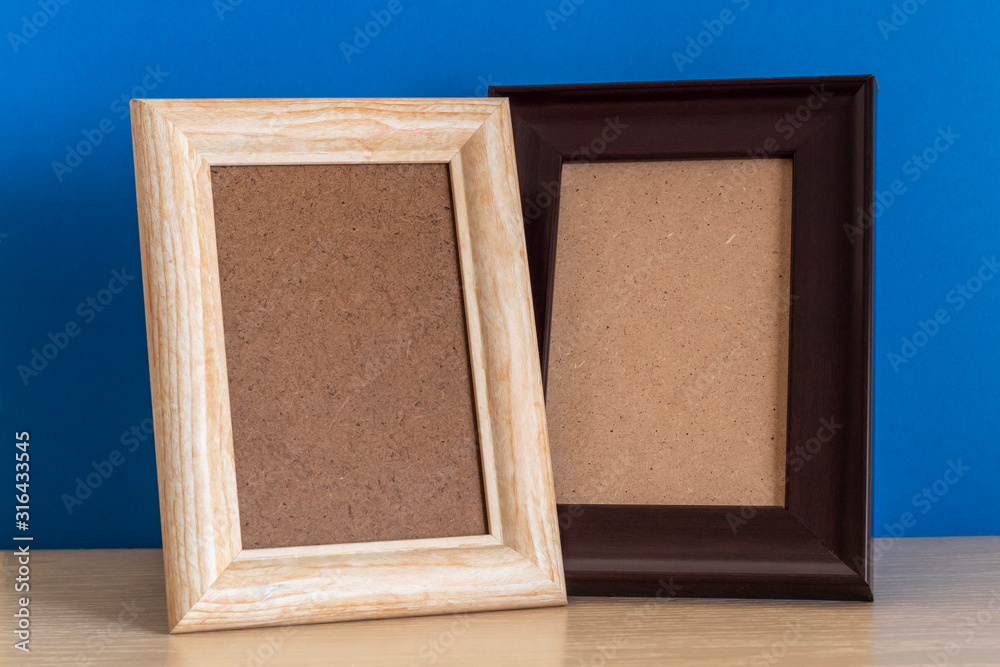 Fototapeta premium Two Empty Wooden Frames on Desk Against Blue Painted Wall