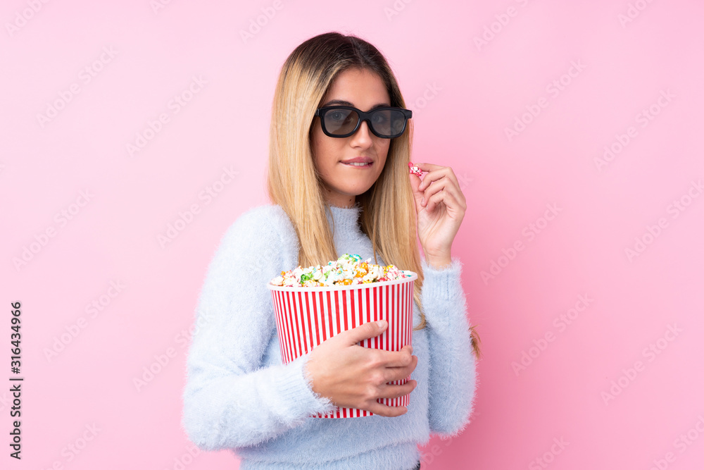 Young Uruguayan woman over isolated pink background with 3d glasses and holding a big bucket of popcorns Young Uruguayan woman over isolated pink background with 3d glasses and holding a big bucket of popcorns