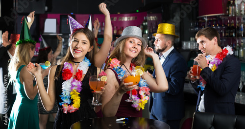 Portrait of young smiling women and men in caps with cocktails
