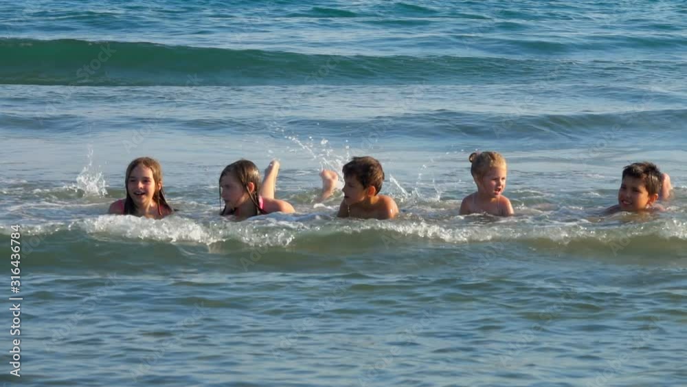 Group of boys and girls are laying on their stomachs in the seashore waves and shaking their legs Group of boys and girls are laying on their stomachs in the seashore waves and shaking their legs