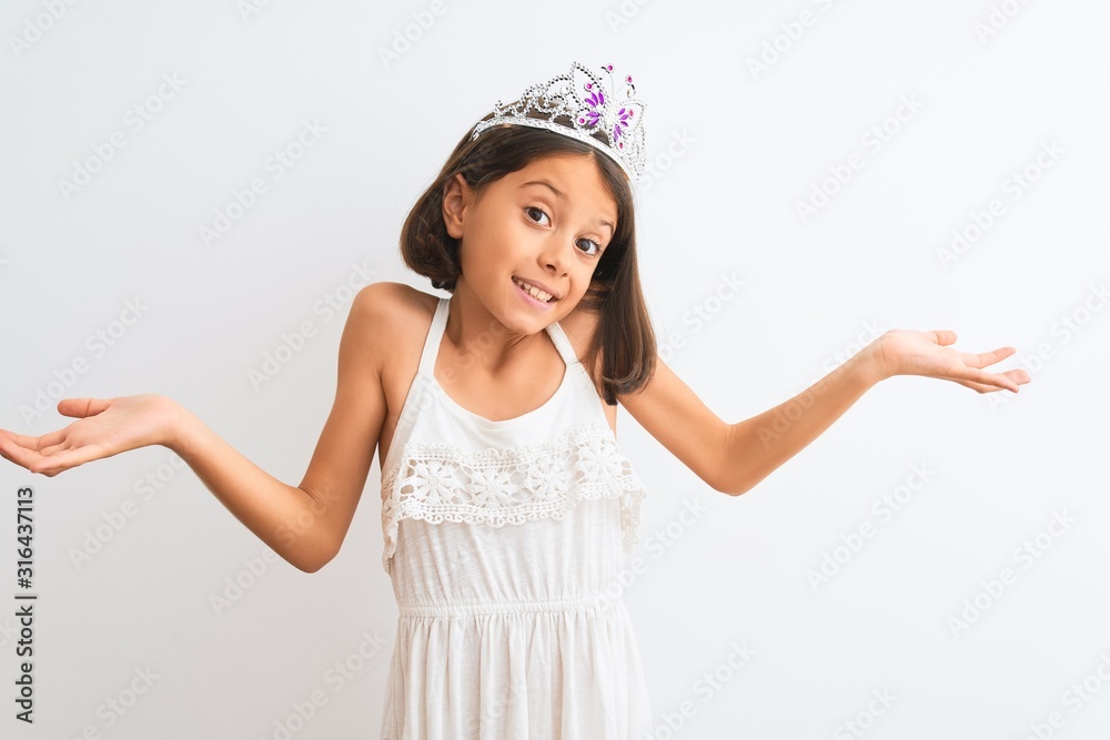 Beautiful child girl wearing princess crown standing over isolated white background clueless and confused expression with arms and hands raised. Doubt concept. Beautiful child girl wearing princess crown standing over isolated white background clueless and confused expression with arms and hands raised. Doubt concept.