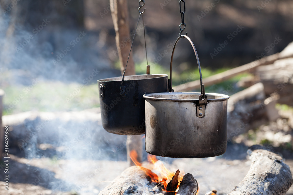 Cooking in two sooty old cauldrons on bonfire with smoke at forest Cooking in two sooty old cauldrons on bonfire with smoke at forest