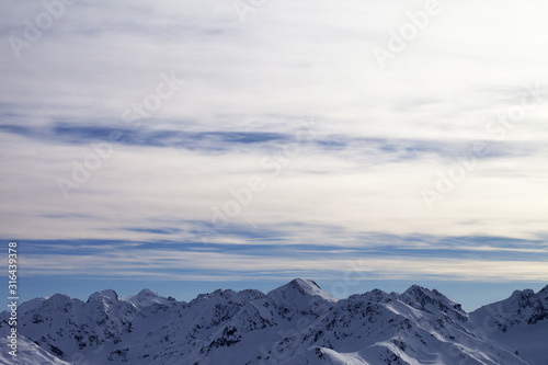 Snowy high mountains and sunlit cloudy sky at winter evening