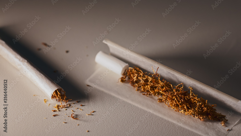 Cigarrillos para liar aislados sobre fondo blanco y luz cálida sobre ellos.  Luz tenue en la escena. Tabaco rubio para liar. foto de Stock