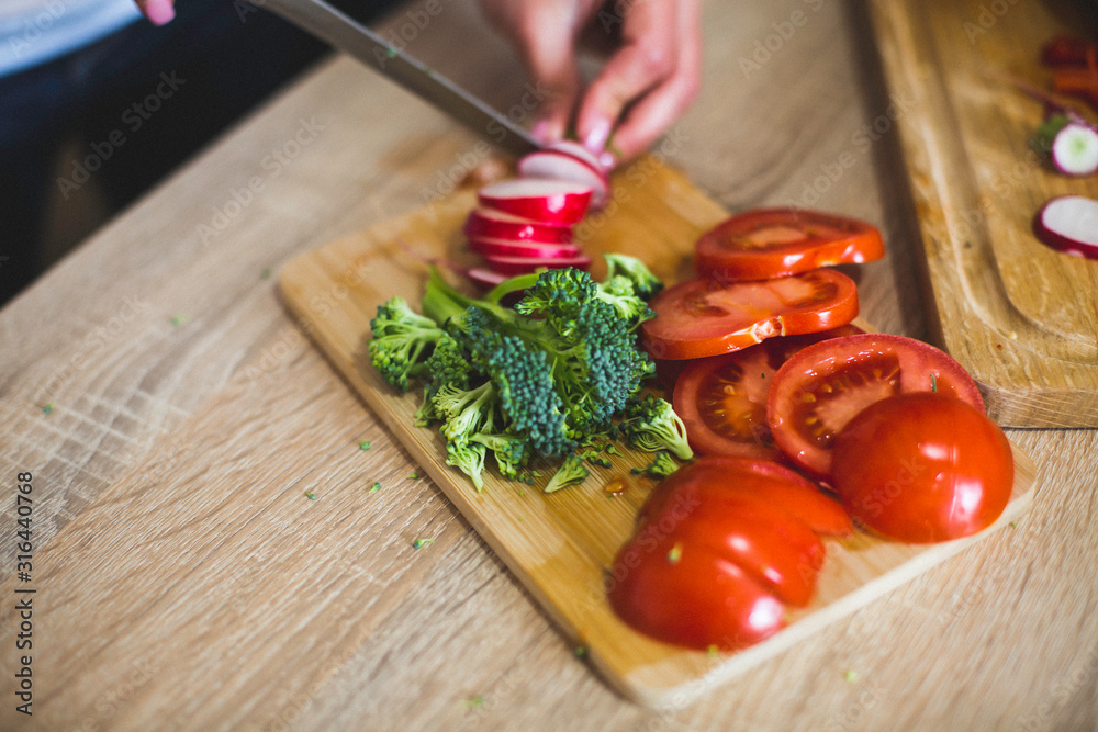 A close-up shop at the cutting board with vegetables, hands and a knife on the kitchen counter. A close-up shop at the cutting board with vegetables, hands and a knife on the kitchen counter.