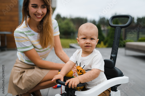 Young mother playing and having fun with her baby boy son brothers in a green garden with cars - Family values warm color summer scene - Eastern European Latvia Riga