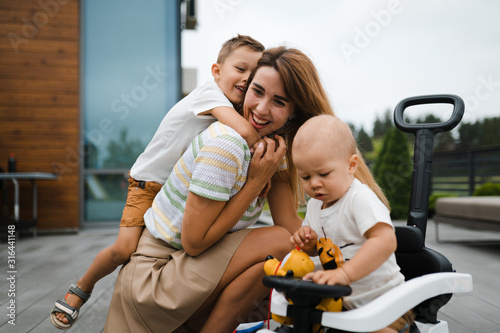 Young mother playing and having fun with her baby boy son brothers in a green garden with cars - Family values warm color summer scene - Eastern European Latvia Riga