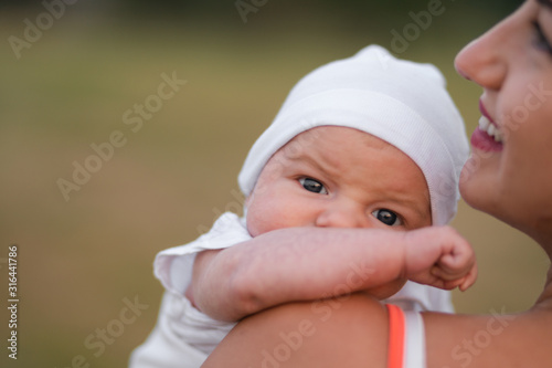 Young mother holding and playing with her baby boy child in city park standing wearing bright red dress - Son wears white cap - Family values warm color summer scene handheld