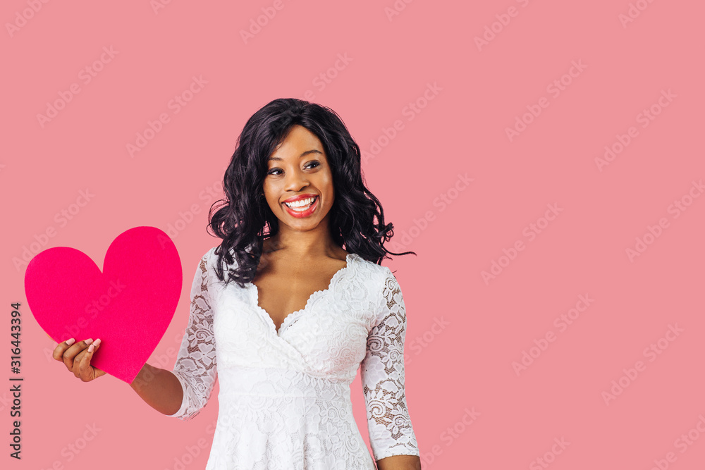 Portrait of young happy woman holding pink heart with big happy smile looking to side, valentineÕs day love Portrait of young happy woman holding pink heart with big happy smile looking to side, valentineÕs day love