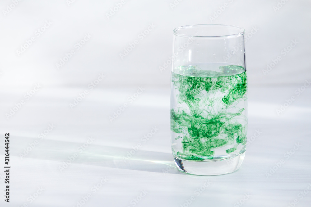 Chlorophyll in glass of water on white wooden background. Copy space, sunlight. Chlorophyll in glass of water on white wooden background. Copy space, sunlight.