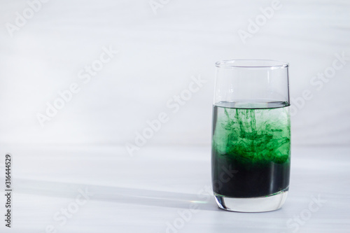 Chlorophyll in glass of water on white wooden background. Copy space, sunlight. photo