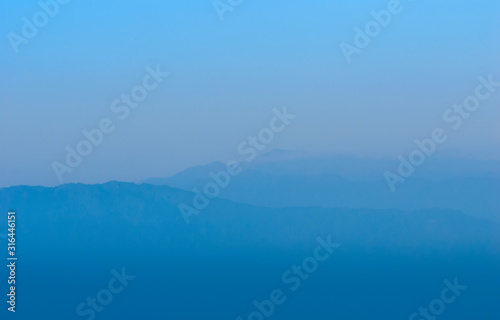 Dark mountains silhouettes covered by the mist and stretching into the distance.