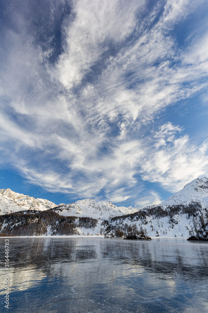 Dramatic clouds over the frozen lake with reflection on the shining solid surface