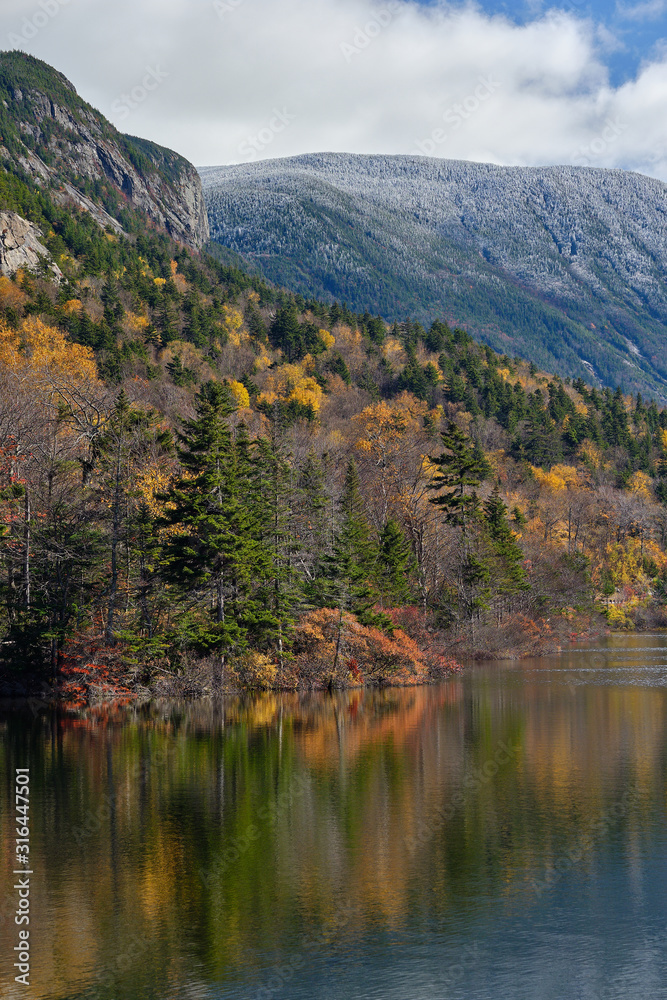 Autumn colors along the shore of Echo lake in New Hampshire with snow and frost on he tops of the White Mountains
