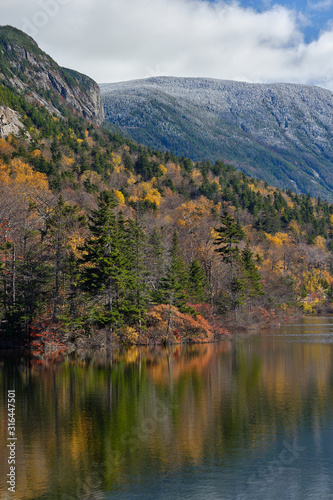 Autumn colors along the shore of Echo lake in New Hampshire with snow and frost on he tops of the White Mountains