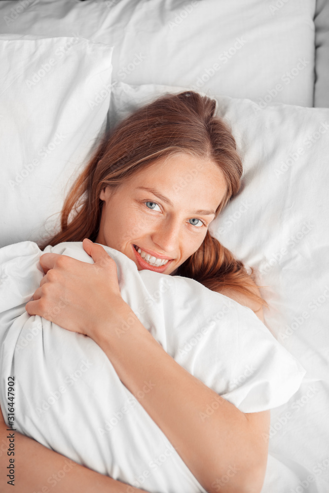 Morning at Home. Woman lying on bed hugging pillow smiling toothy top view close-up