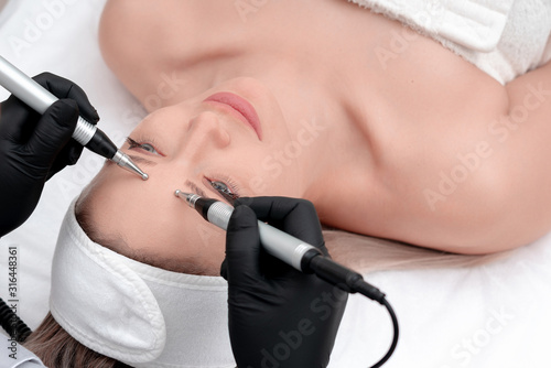 Cosmetology. Beautiful Woman At Spa Clinic Receiving Stimulating Electric Facial Treatment From Therapist. Closeup Of Young Female Face During Microcurrent Therapy photo