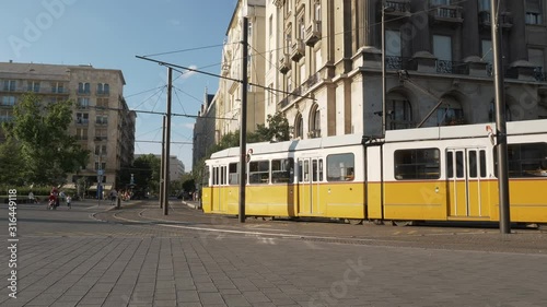 Tram crossing in front of Budapest Parliament, with people walking around. Dolly shot