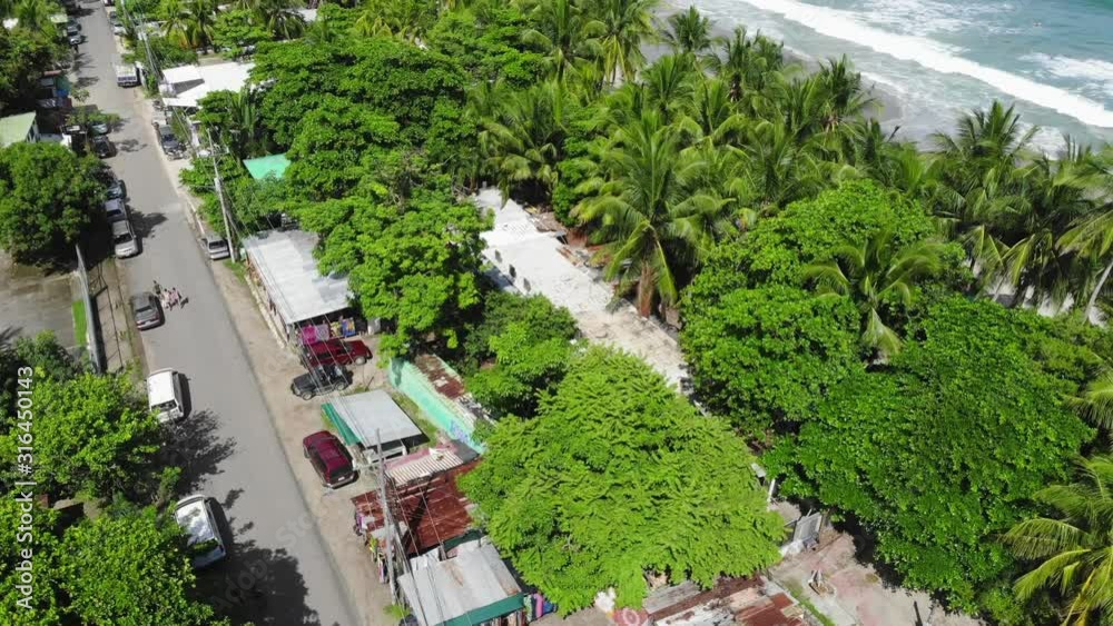 Aerial shot flying upwards from the village of Samara, shot towards the beach and the sea, including palm trees and sunny weather. Shot includes some moving traffic. Samara, Costa Rica. Aerial shot flying upwards from the village of Samara, shot towards the beach and the sea, including palm trees and sunny weather. Shot includes some moving traffic. Samara, Costa Rica.