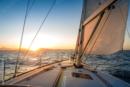 Chasing the sun at sailing yacht. Deck and sails of sailoat pointing to the sunrise. Mediterranean sea, Italy. © AlexanderNikiforov