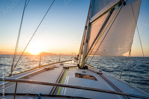 Sailing yacht navigationg to the sun rising on the horizon.. Mediterranean sea, Italy. © AlexanderNikiforov