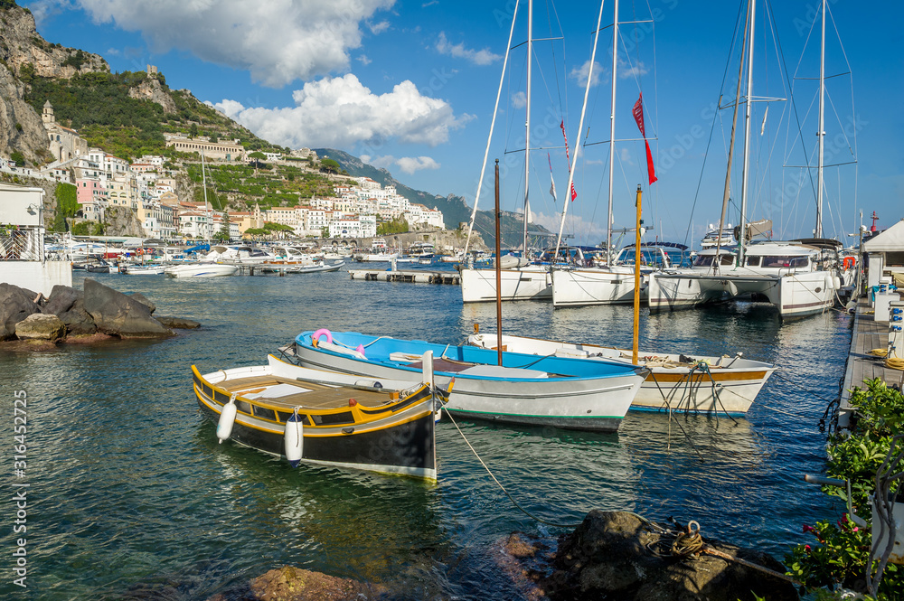 Traditional boats and modern yachts docked at Amalfi marina, Italy.