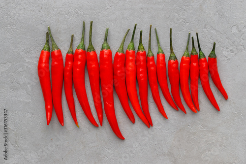 Flat lay composition a row of red hot chilli peppers on light concrete background. Spicy capsicum peppers wallpaper pattern. 