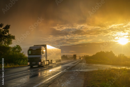 During an evening summer showers. A bright sun sunshine through thunderstorm clouds over the highway. Trucks and passenger cars go on the wet asphalt. Montage or graphic software was not used