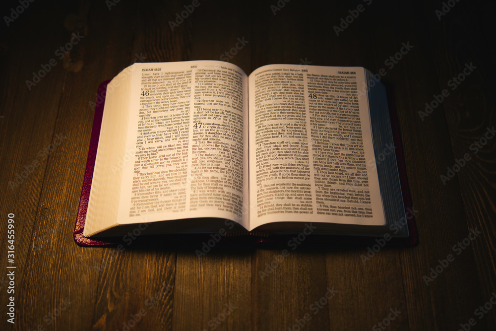Obraz premium Open Holy Bible over a wooden table at night