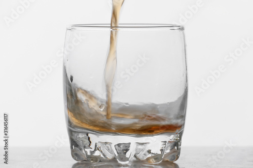 Process of filling glass by whiskey on white background