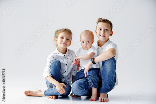 Happy sisters and brother are sitting on the floor on a white background. Two teens and a baby 1 year. photo