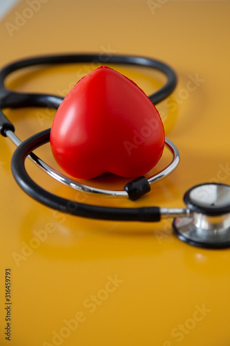 Stethoscope doctors and red heart cardiology placed on a Yellow table in the hospital, photo