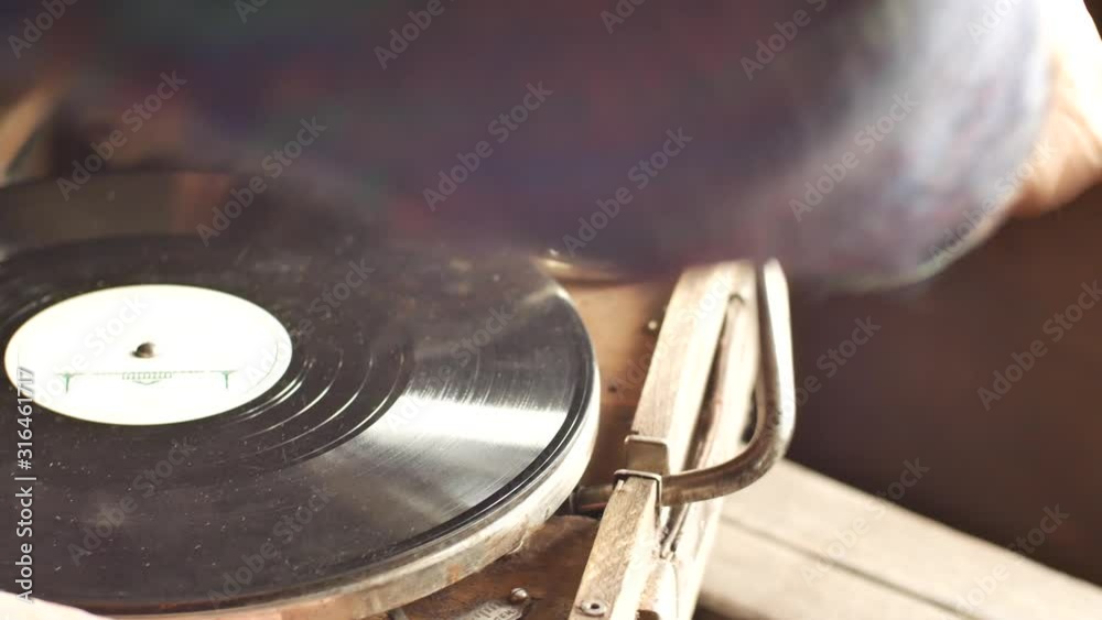 Person puts a record on an old gramophone. Turns it on with a special handle. Vintage interior items.