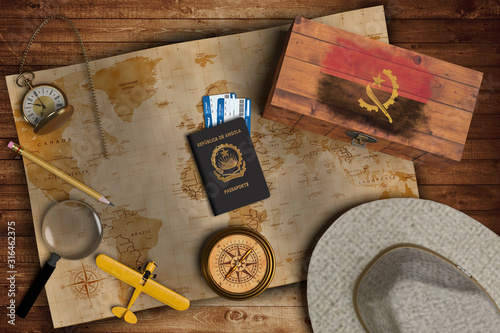 Top view of traveling gadgets, vintage map, magnify glass, hat and airplane model on the wood table background. On center, official passport of Angola and your flag.